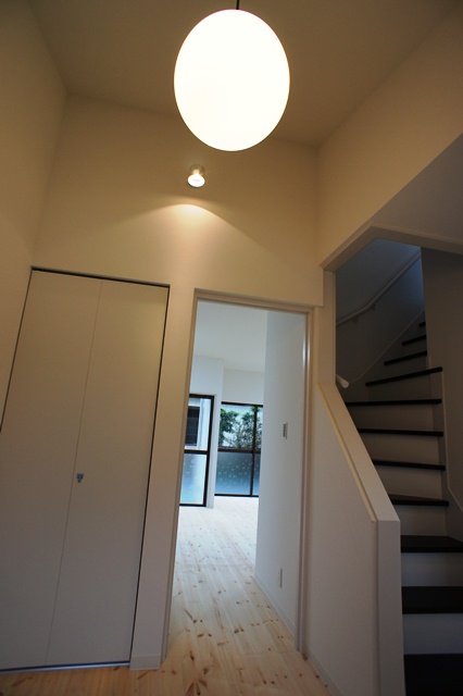 爽やかな白の壁と無垢の床材がいい感じ、玄関はリノベで極力高さを取るように勾配天井にして上から特徴のある照明器具でお客様を迎えます。