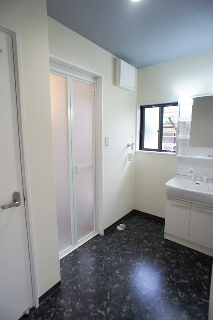 キッチン横からのアクセス可能な洗面スペース。写真左奥はユニットバス、写真左手前のドアはトイレのドア。家の全体的には白色のクロスにフローリングなので、洗面スペースは天井に藍と床は黒っぽい色をチョイス。
